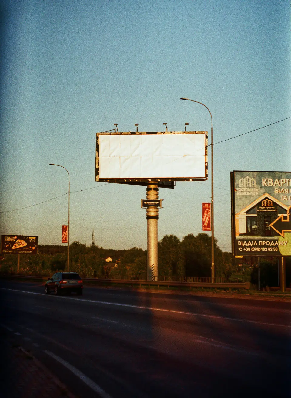 Blank billboard above a roadside at dusk